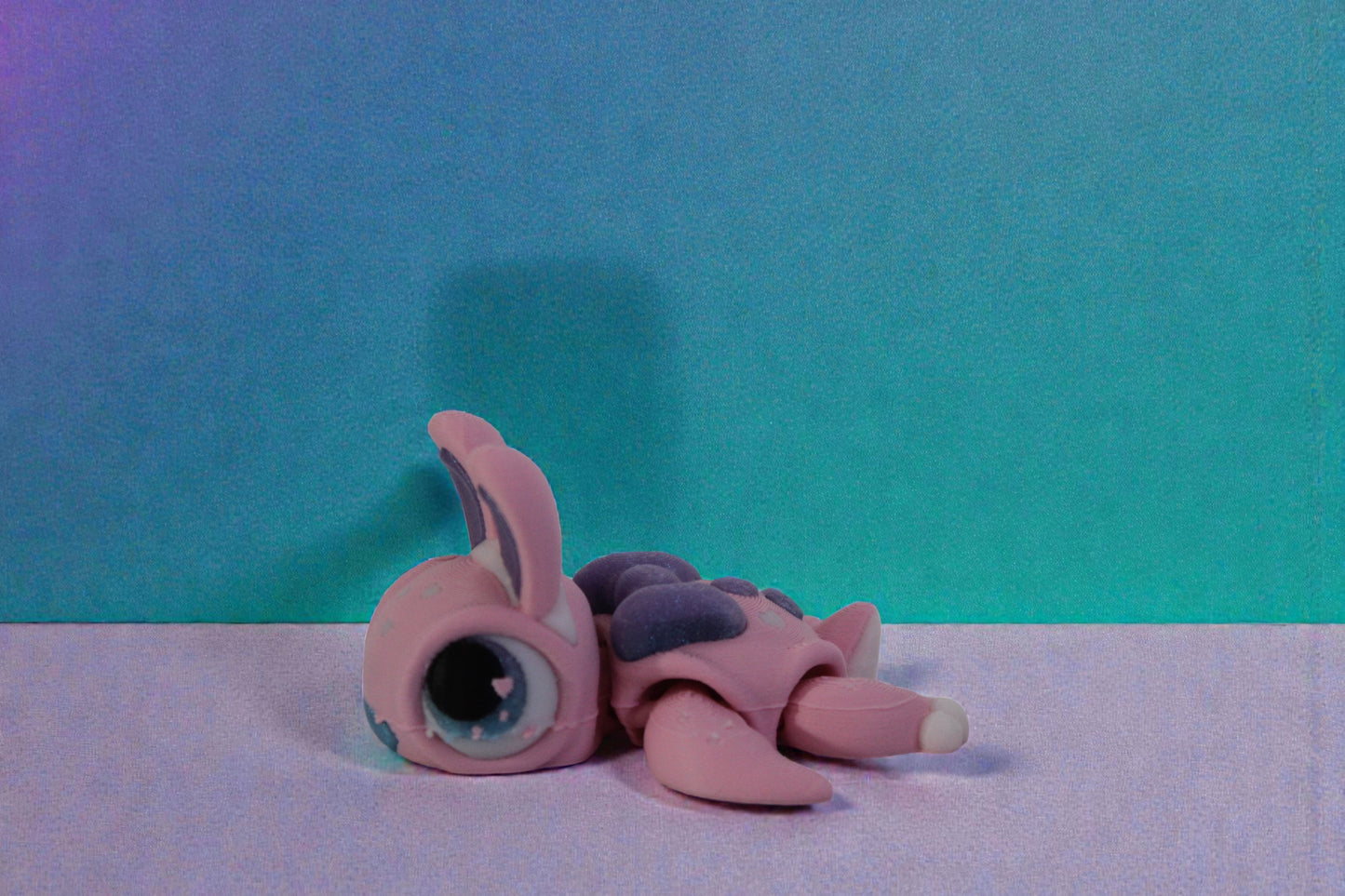 Low side profile of the 3D printed pastel bunny turtle posed flat on a clean white surface.