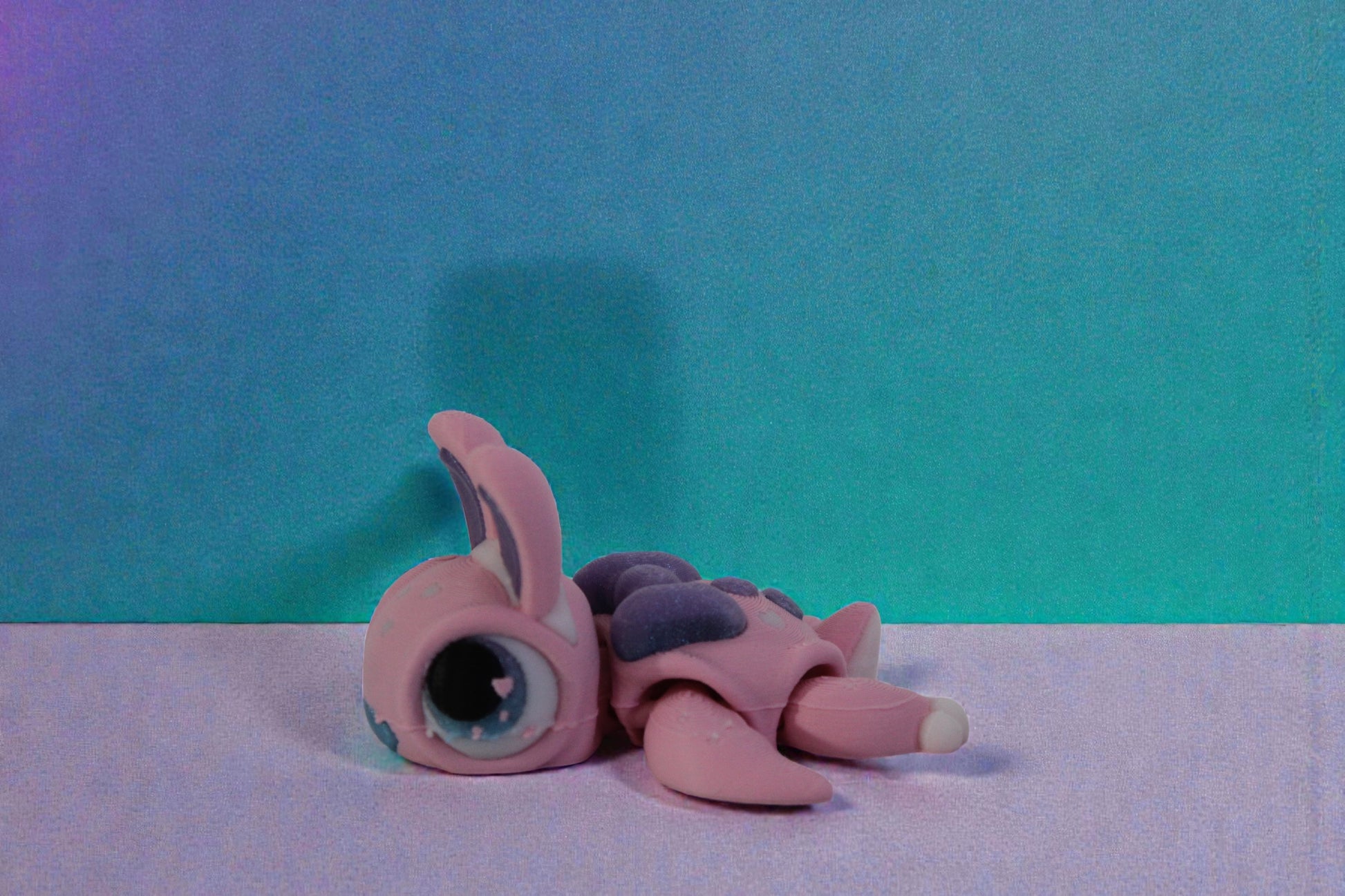 Low side profile of the 3D printed pastel bunny turtle posed flat on a clean white surface.