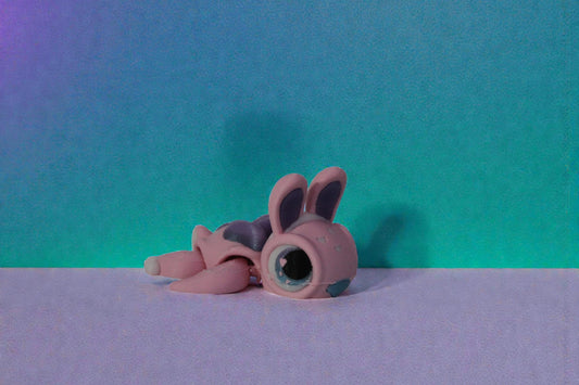 Side angle view of a pastel pink articulated bunny turtle with shimmer purple shell and large glossy eyes on a neutral background.