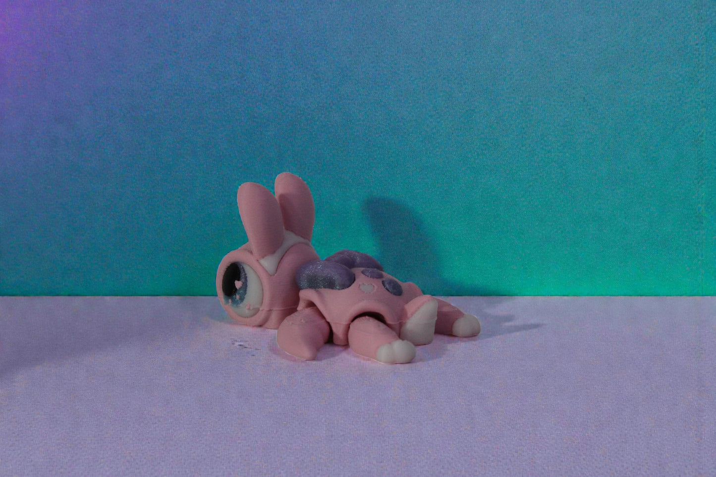 Side angle view of a pastel pink articulated bunny turtle with shimmer purple shell and large glossy eyes on a neutral background.
