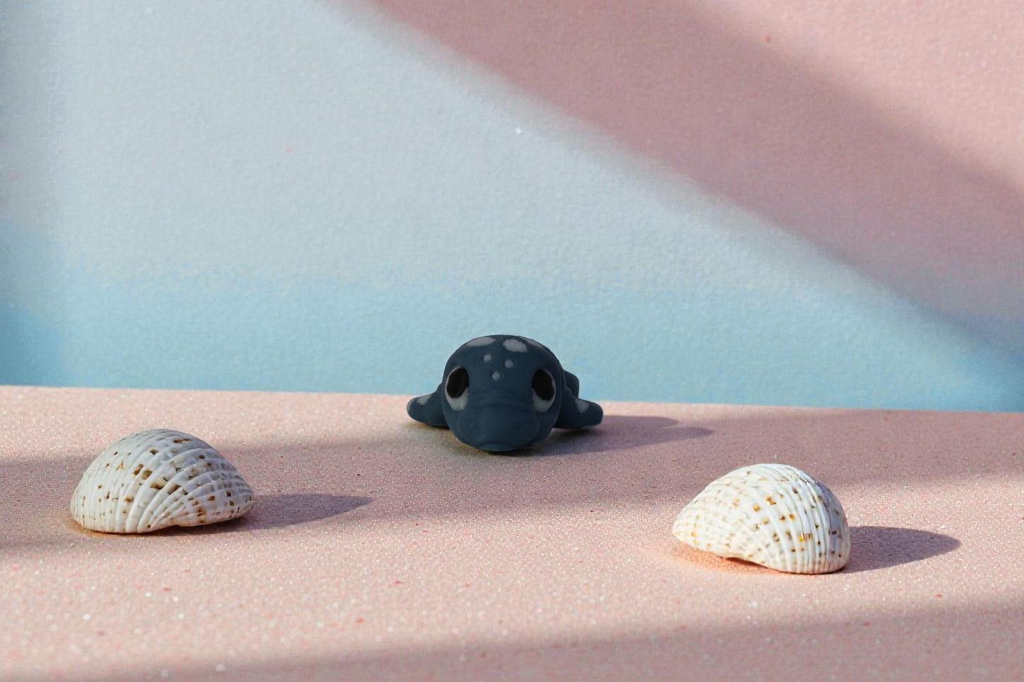 Front facing mini articulated water dragon collectible in matte denim blue PLA, 3D printed in small batches, displayed between seashells on soft pastel sand, affordable fantasy decor for dragon collections and shelf styling.
