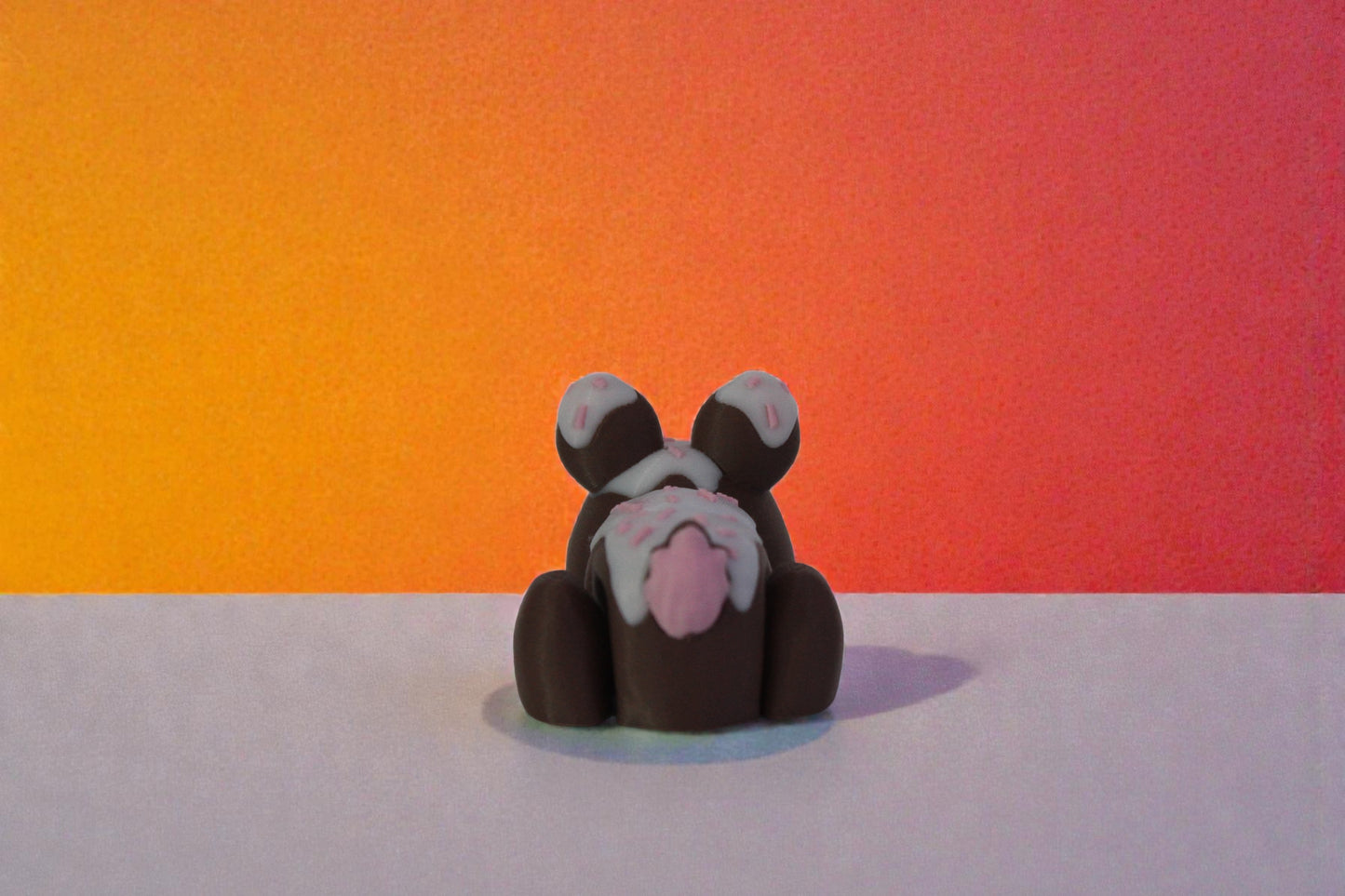 Rear view of mini chocolate glaze bunny decor showing white icing drip and pink sprinkle details across the back, small batch 3D printed collectible.