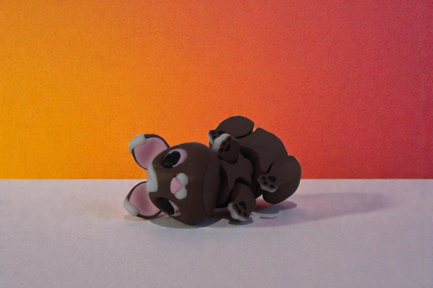 Articulated chubby bunny figurine lying on its side to show segmented body and paw details, chocolate brown with white glaze accents, 3D printed PLA decor.