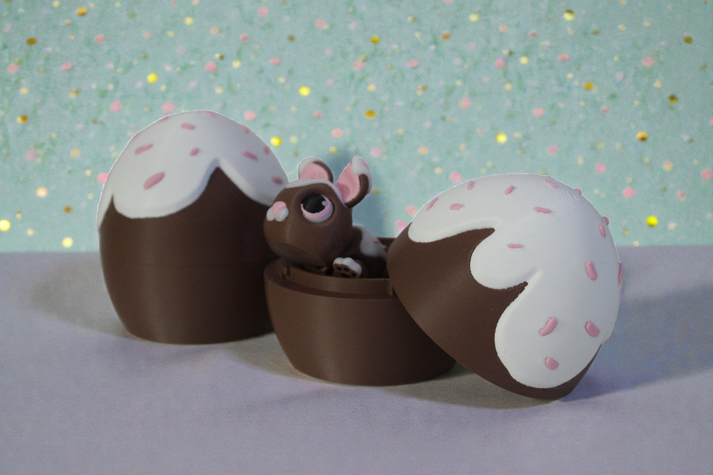 3D printed chocolate glaze locking egg container open with bunny inside, brown PLA base with white drip top and pink sprinkle details, decorative Easter shelf display.