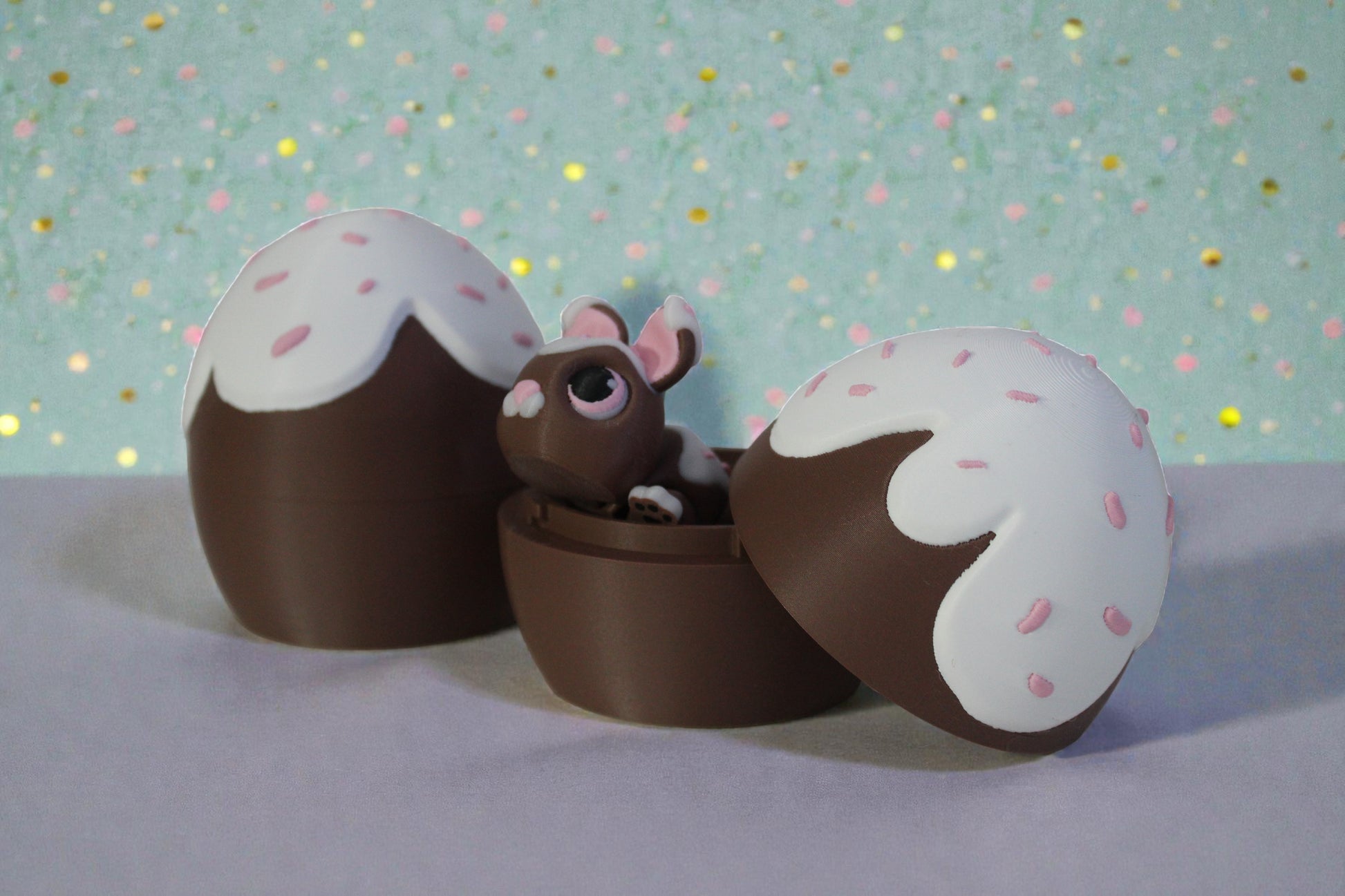 3D printed chocolate glaze locking egg container open with bunny inside, brown PLA base with white drip top and pink sprinkle details, decorative Easter shelf display.
