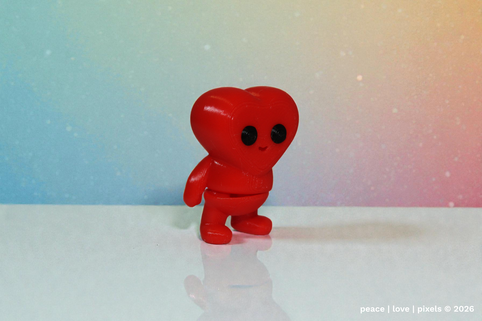 3D printed, red heart-shaped articulated figure with black eyes on a white surface and gradient background. Designer: ZOU3D. peace | love | pixels is an authorized seller for ZOU3D. https://www.instagram.com/zou3d