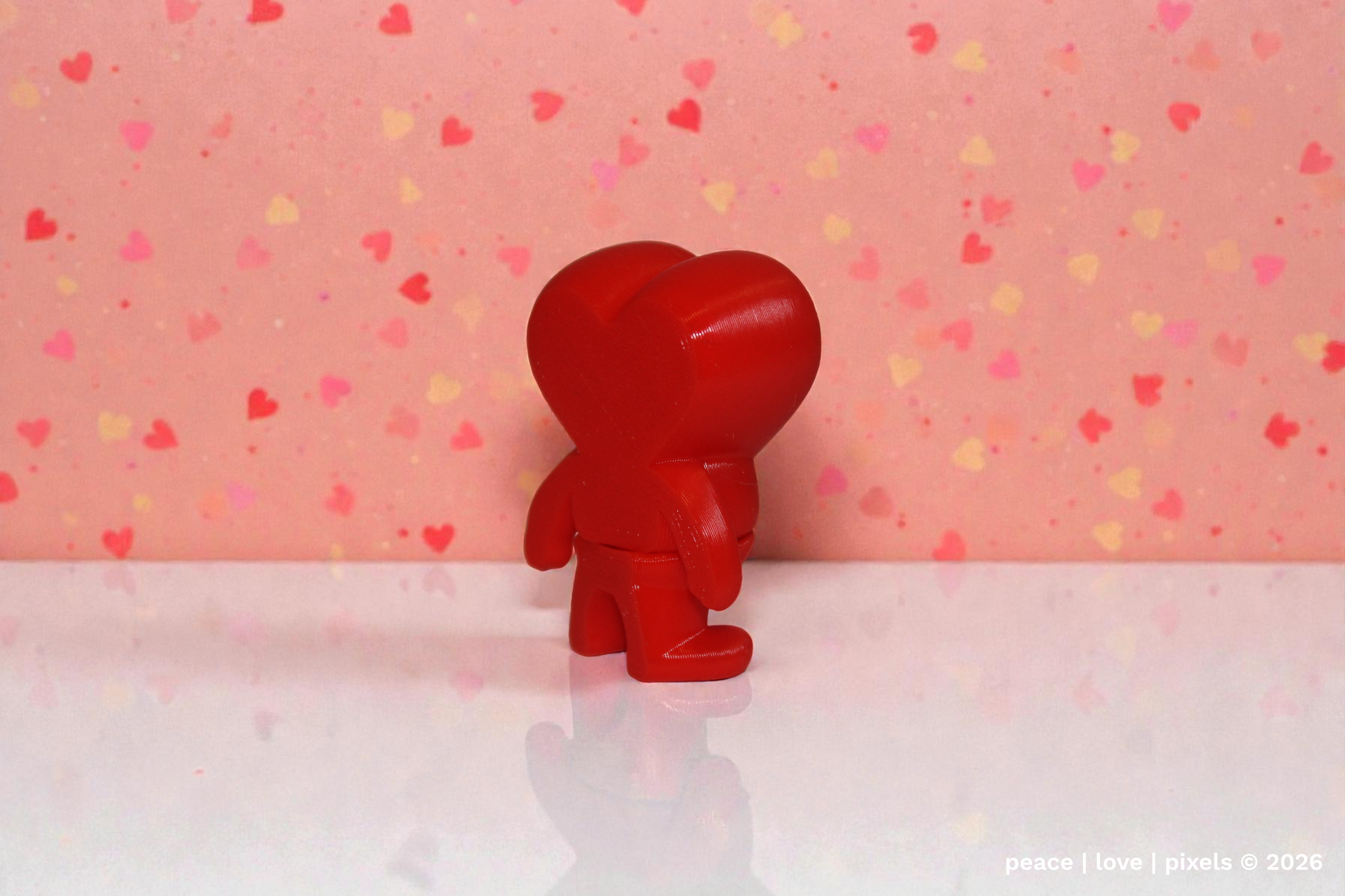 Red, gently articulated, heart figurine on a white surface with a pink background featuring heart patterns. Designer: ZOU3D. peace | love | pixels is an authorized seller for ZOU3D. https://www.instagram.com/zou3d